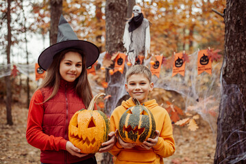 Happy boy and girl children with pumpkins in autumn forest decorated for Halloween. Celebrating...