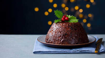 Christmas pudding, fruit cake. Traditional festive dessert. Dark background with lights garland. Close up. Copy space.