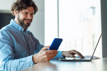Portrait of smiling man using smartphone and pc at office