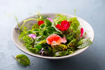 Foto op Canvas Green salad leaves, sprouts with edible flowers in bowl. Grey background. Close up. © annapustynnikova