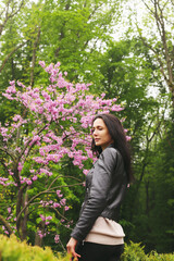 A girl poses on the street near a flowering tree.