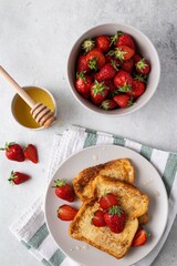 Traditional french toasts with strawberries and honey on grey background. Summer breakfast, brunch or lunch with berries. Top view.