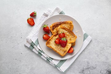 Traditional french toasts with strawberries and honey on grey background. Summer breakfast, brunch or lunch with berries. Top view.