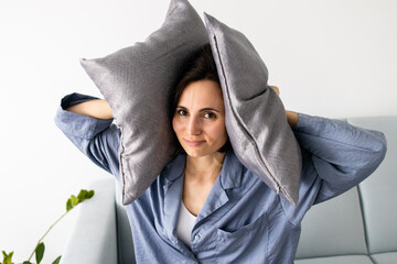 Close up of woman's face covering her ears with a pillows who is frustrated by noise of neighbors. ...