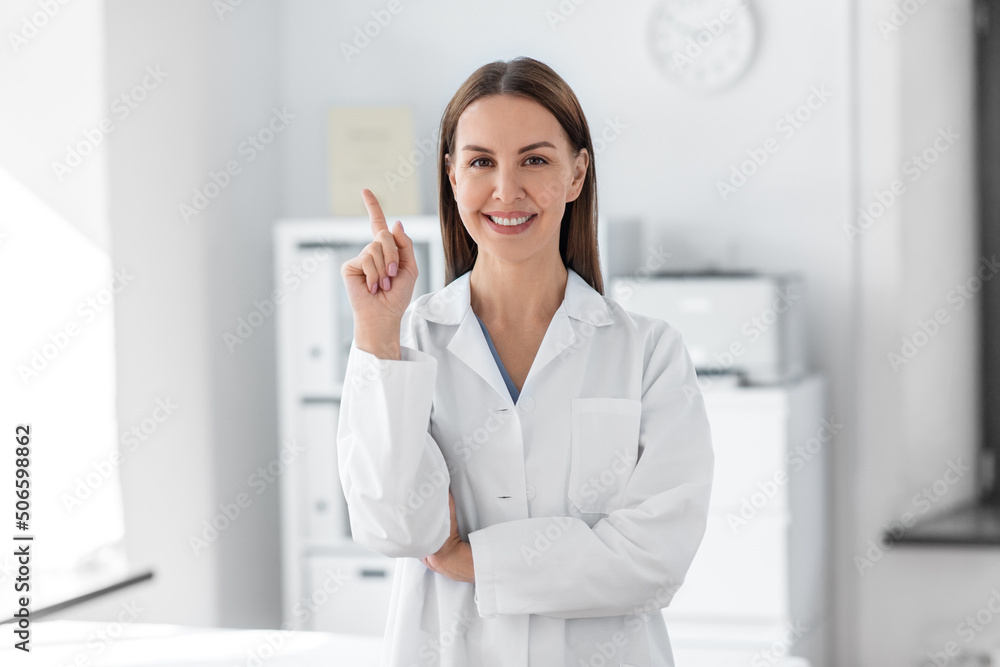 Wall mural medicine, healthcare and profession concept - smiling female doctor pointing finger up at hospital