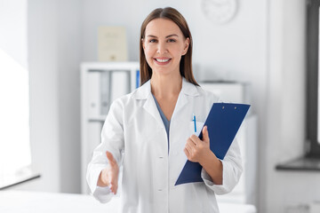 medicine, healthcare and profession concept - smiling female doctor with clipboard giving her hand for handshake at hospital
