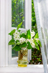a bouquet of white lilac flowers in a glass vase on a white windowsill at an open window in a village house