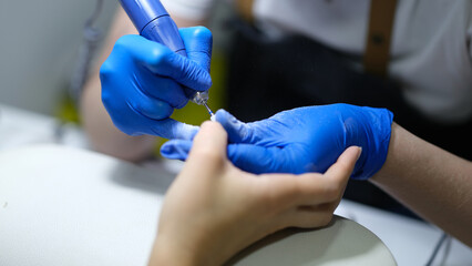 Manicurist uses electric manicure machine to remove nail polish from hands in nail salon