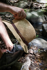 Mano cogiendo gorrro de paja en bosque, excursión junto al río en vacaciones de verano