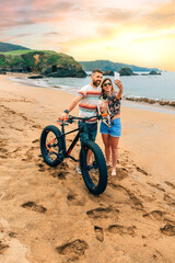 Fototapeta premium Young couple with fat bike taking a selfie with their dog on the beach