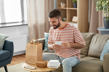 communication, leisure and people concept - happy smiling man with bill checking takeaway food order at home