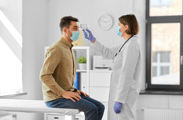 medicine, healthcare and people concept - female doctor in mask with infrared forehead thermometer measuring temperature of man patient at hospital