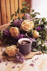 Bouquet of purple lilacs with yellow roses. Gray cup of coffee. Romantic spring flowers. Side view on window background.