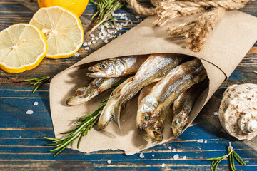 Sun-dried smelt in a paper package. Salted fish with marine decor. Lemon, fresh rosemary, sea rope