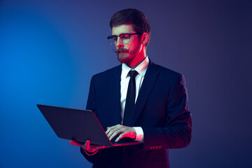 Portrait of young stylish serious man in business suit working remote isolated on dark blue studio background. Concept of emotions, work, sales, ad, fashion and beauty