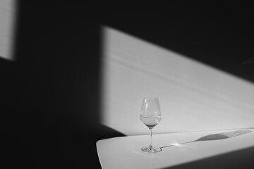 A glass of white wine on a white background with a shadow. Chiaroscuro from the window. Black and...