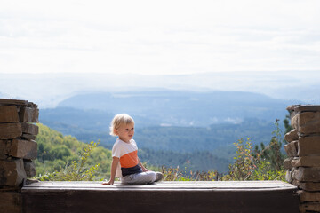 Fototapeta premium rear view blonde kid boy sitting outdoors on the bench and enjoying beautiful nature view
