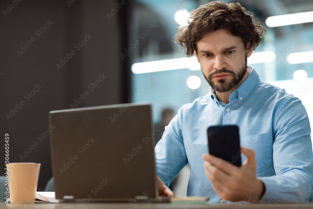 Poster portrait of focused man using smartphone and pc at office