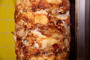 Skewered roasted chicken shawarma meat cooking and turning on rotating spit in fast food restaurant.