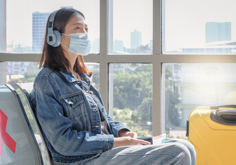 Happy lone Asian female traveler wearing protective face mask, relax listening music, sitting...
