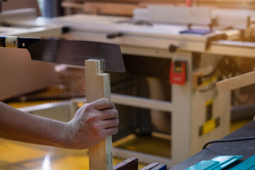 Professional carpenter man is sawing a wooden beam in woodwork industry. The worker makes a cut on a  saw.