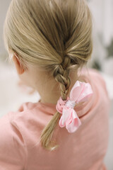 Obraz na płótnie Canvas Blonde little girl braid hair with pink ribbon bow. Haircare, hairstyling.