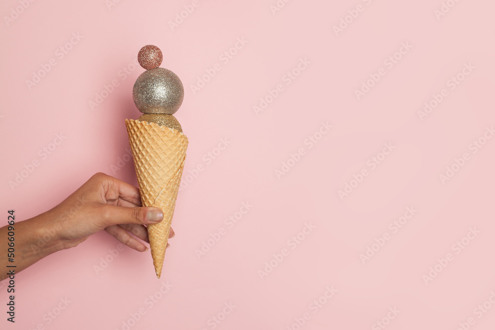 Wall mural christmas ice cream. waffle cone with xmas balls decoration in female hand on pink banner background