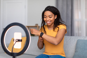 Blogging concept. Happy african american female video blogger with cellphone on ring lamp recording...