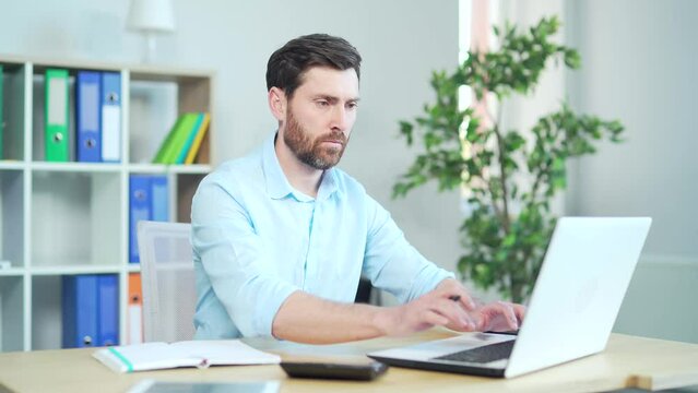 Man watching video course on business. Online education, e-learning. Caucasian confident guy sitting at a work desk, uses laptop computer, listening online lecture, taking notes, at workplace office.