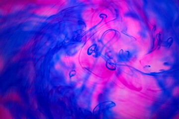 Shallow depth of field shot of swirling pink and blue ink in water - soft flowing abstract and...