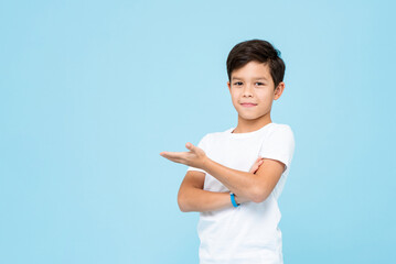 Cute smiling boy in plain white t shirt opening empty hand in isolated studio light blue color...