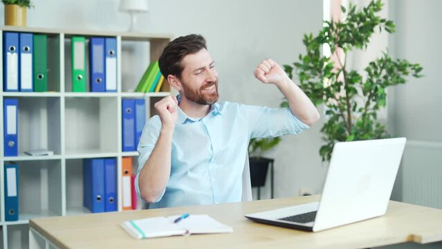 Happy and cheerful office worker dancing at work sitting at a computer desk. enjoy after successful agreement. employee business man in shirt Handsome funny Bearded Manager rejoices in the work done