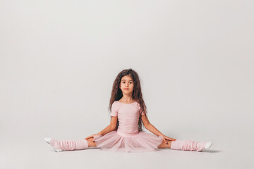 Obraz na płótnie Canvas Little swarthy ballerina dancer in a pink tutu academy student posing on white background 