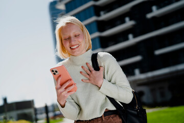 Happy girl walking on the street checking phone. Beautiful blonde girl enjoy in sunny day.
