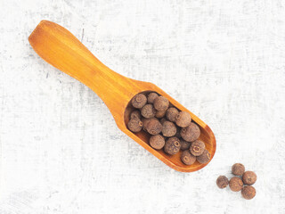 Spice Allspice (Jamaica pepper, Pimento) in wooden scoop, bunch on white concrete background. Macro. Flat lay. Indian cuisine concept