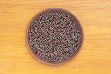 Spice Mustard seeds (Brassica juncea) in brown clay plate on yellow wooden background. Close up. Vegetarian food concept
