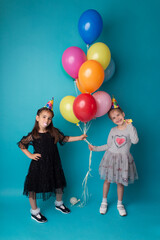 Smiling adorable little child girls posing with color air balloons on blue background. Beautiful happy kid on a birthday party