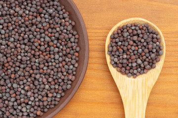 Mustard in clay plate and wooden spoon on brown wooden background. Healthy diet concept