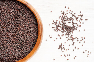 Mustard seeds in wooden bowl and scattered on white wooden background. Close up. Vegetarian food concept