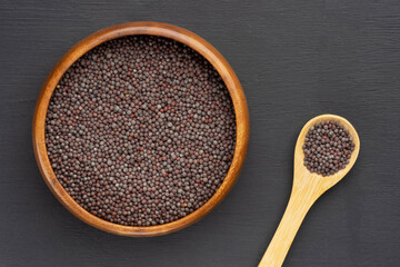 Spice Mustard seeds (Brassica juncea) in wooden bowl and spoon on black wooden background. Macro....