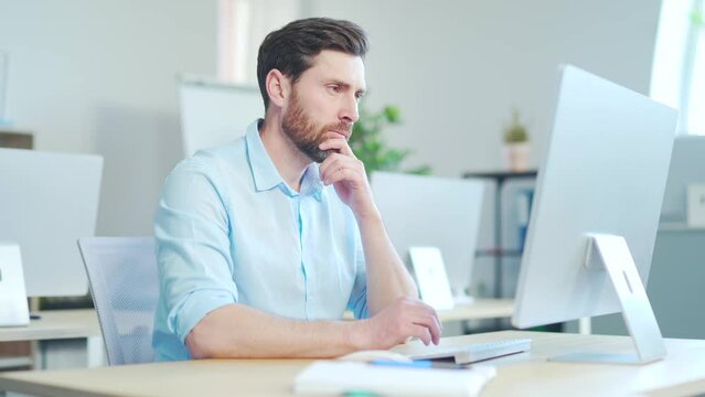 Focused bearded business man entrepreneur typing on laptop pc computer doing research. Young male professional using computer sitting at modern office desk. Busy worker working on modern tech notebook