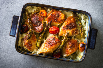 Baked chicken thighs with asparagus and tomatoes in a creamy sauce.