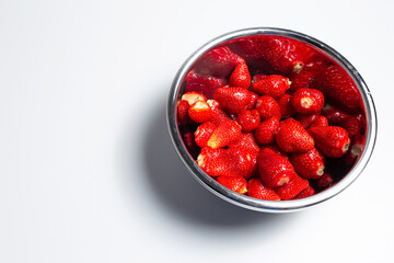 Close-up of steel bowl with strawberries on white background with copy space.