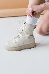 Cropped view of woman in boot adjusting sock on beige background.