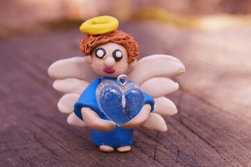 A toy angel made of plasticine with a heart in his hands. A symbol of hope, happiness and well-being.