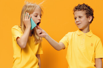 cute, funny children, brother and sister of school age are standing in bright clothes on a yellow background and the girl is talking on the phone