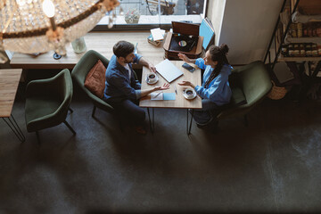 View from above on mixed-races friends or colleagues talking at table with coffee in cafe. Top view.