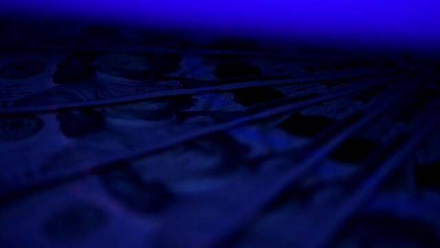A lot of hundred-dollar bills under the ultraviolet light slowly rotates in a circle.