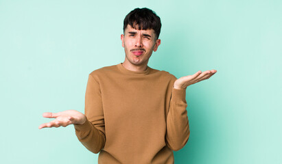 young adult hispanic man looking puzzled, confused and stressed, wondering between different...
