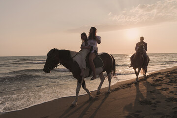 The family spends time with their children while riding horses together on a sandy beach. Selective focus 